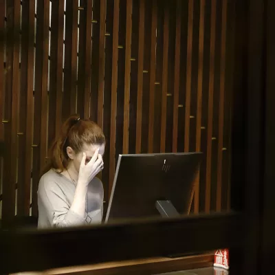 A woman sitting in front of a computer screen with her hand at her forehead